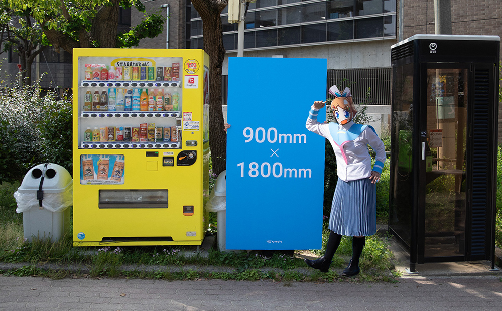 自動販売機とサブロクサイズの発泡パネルを横に並べ、サイズ感を紹介しているソクプリ子ちゃん