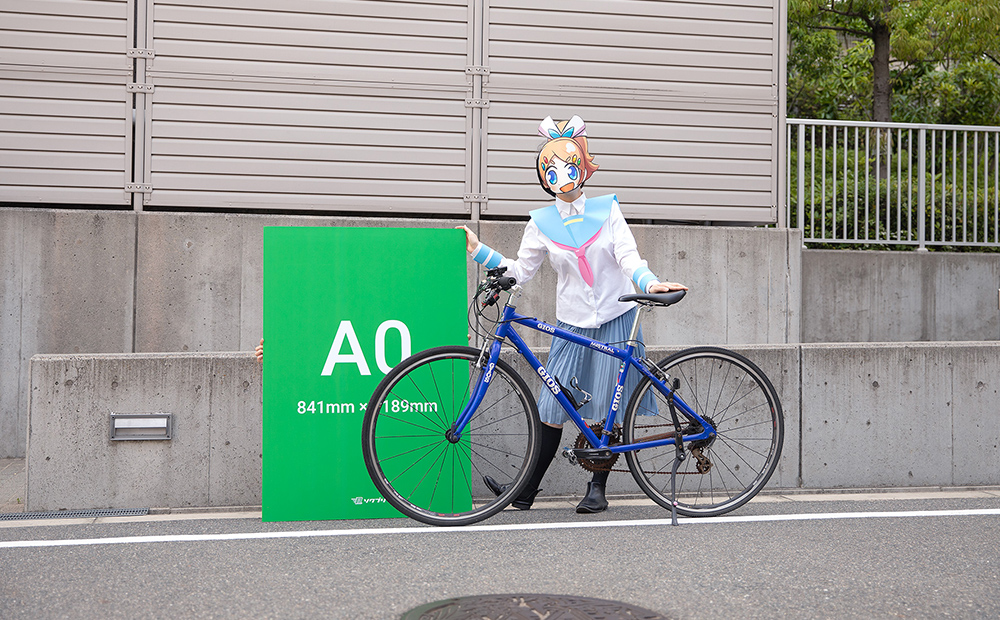 A0サイズの発泡パネルとクロスバイクのサイズを比べているソクプリ子ちゃん